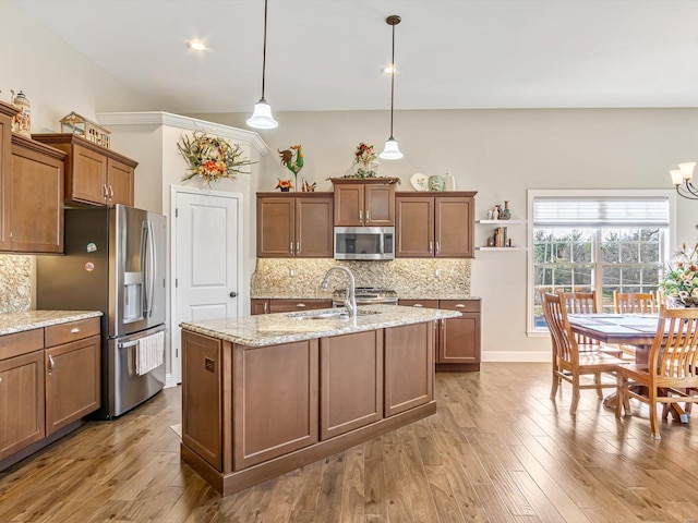 kitchen with appliances with stainless steel finishes, an island with sink, sink, hanging light fixtures, and light stone counters