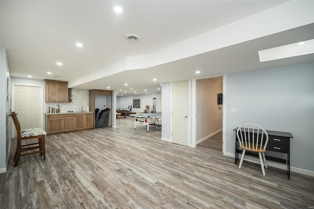 kitchen featuring baseboards, brown cabinets, wood finished floors, backsplash, and recessed lighting