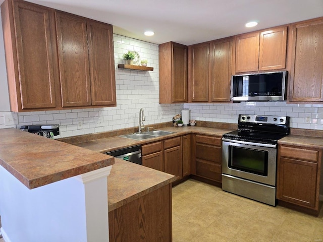 kitchen featuring brown cabinetry, appliances with stainless steel finishes, a peninsula, a sink, and backsplash