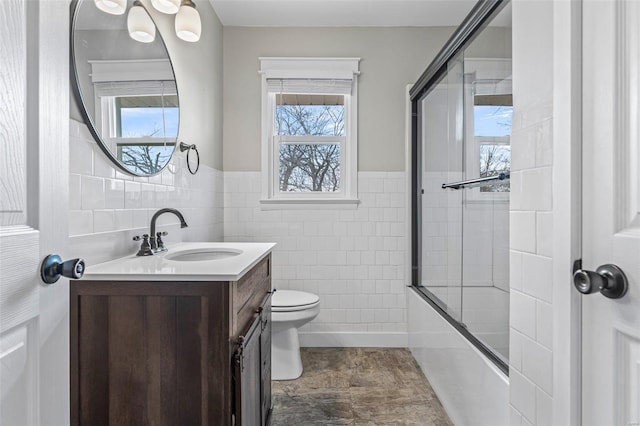 full bathroom featuring toilet, vanity, bath / shower combo with glass door, and tile walls