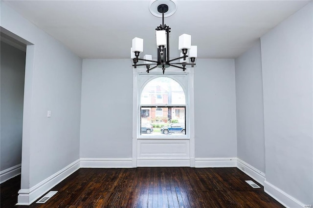 empty room with dark wood-type flooring and a notable chandelier