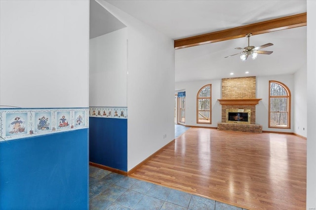 unfurnished living room with lofted ceiling with beams, hardwood / wood-style flooring, a brick fireplace, and a healthy amount of sunlight