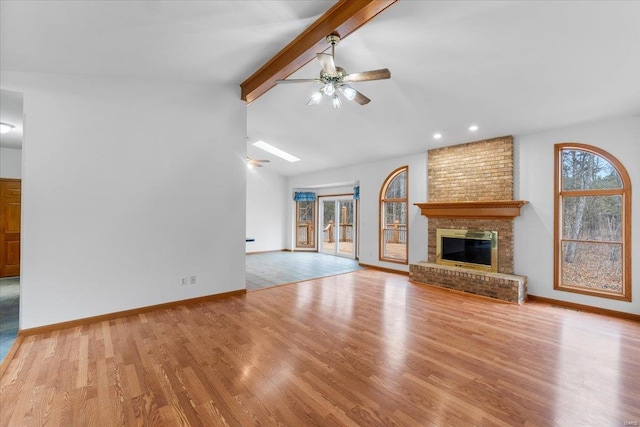 unfurnished living room with a brick fireplace, light hardwood / wood-style flooring, lofted ceiling with beams, and ceiling fan