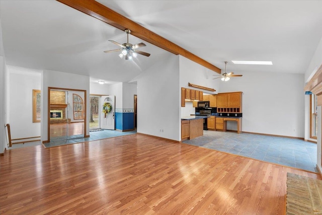 unfurnished living room featuring beam ceiling, a skylight, light wood-type flooring, ceiling fan, and a fireplace