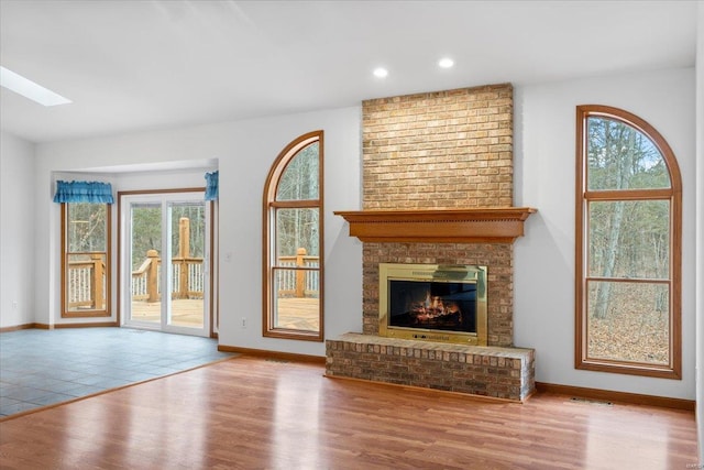 unfurnished living room with plenty of natural light, a fireplace, a skylight, and light hardwood / wood-style floors