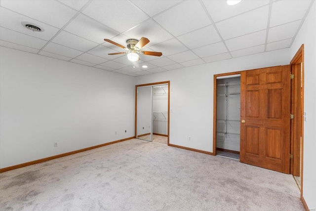 unfurnished bedroom with multiple closets, a paneled ceiling, light colored carpet, and ceiling fan