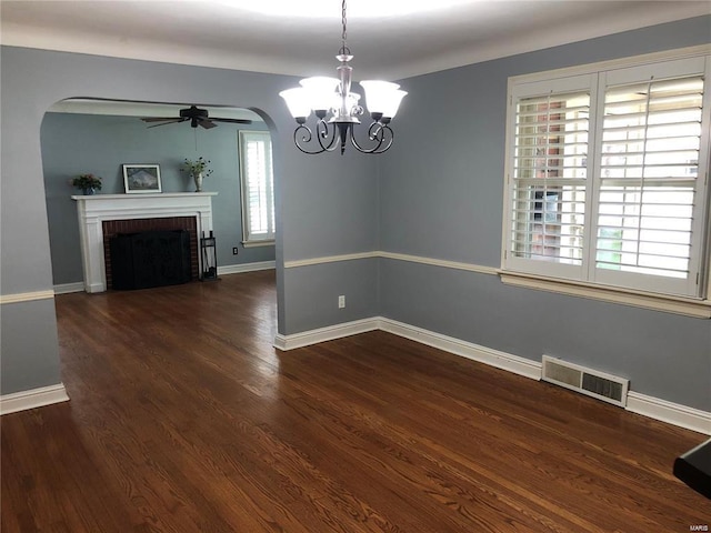 unfurnished dining area featuring dark hardwood / wood-style flooring, ceiling fan with notable chandelier, and a fireplace