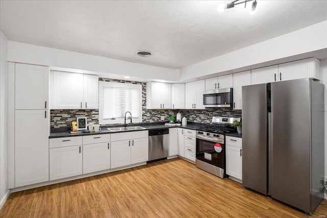 kitchen featuring light wood finished floors, stainless steel appliances, dark countertops, visible vents, and a sink