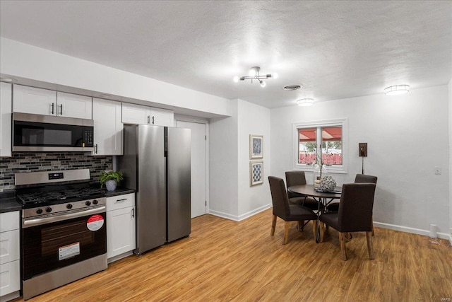 kitchen with appliances with stainless steel finishes, dark countertops, light wood finished floors, and tasteful backsplash