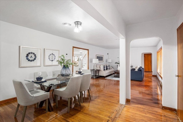 dining room with arched walkways, stairs, light wood-style flooring, and baseboards