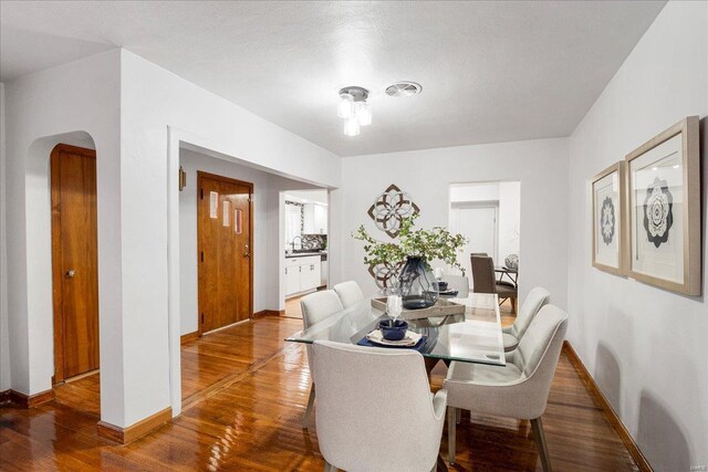 dining area with arched walkways, baseboards, and wood finished floors