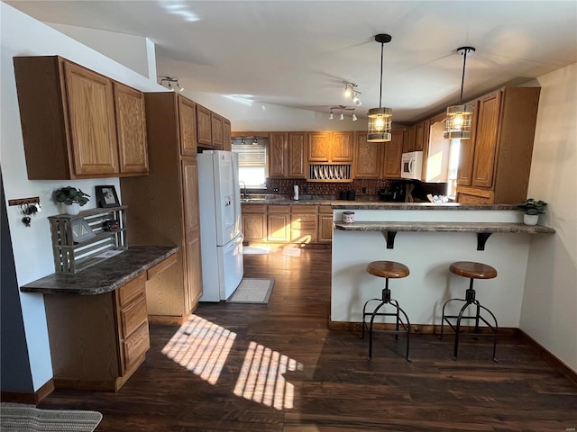 kitchen featuring pendant lighting, tasteful backsplash, a kitchen bar, dark wood-type flooring, and white appliances