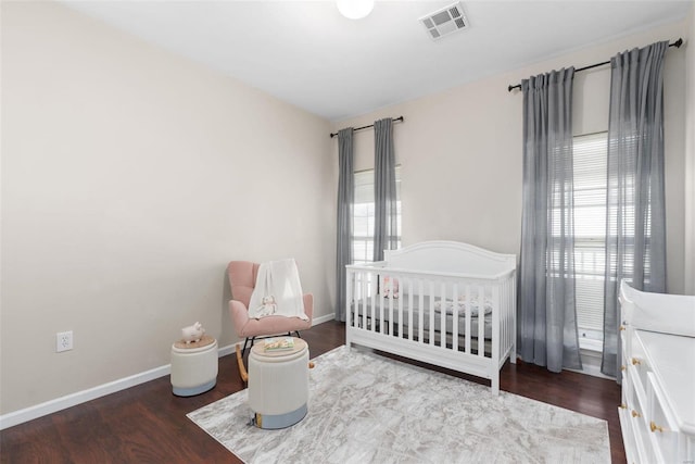 bedroom featuring multiple windows, hardwood / wood-style floors, and a crib