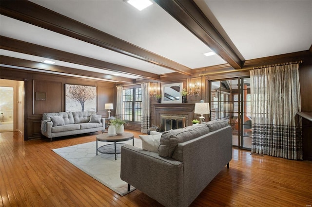 living area featuring a glass covered fireplace, beam ceiling, and wood-type flooring