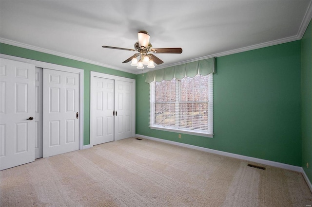 unfurnished bedroom with baseboards, visible vents, two closets, and ornamental molding