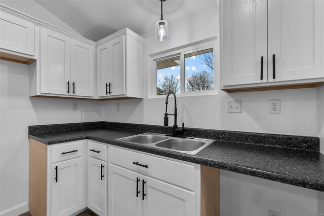 kitchen with a sink, white cabinets, vaulted ceiling, dark countertops, and decorative light fixtures