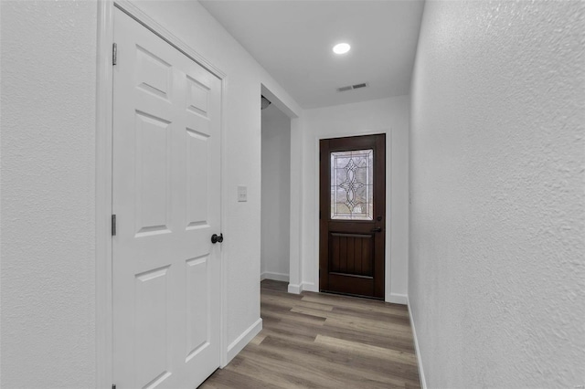 doorway to outside featuring a textured wall, wood finished floors, visible vents, and baseboards