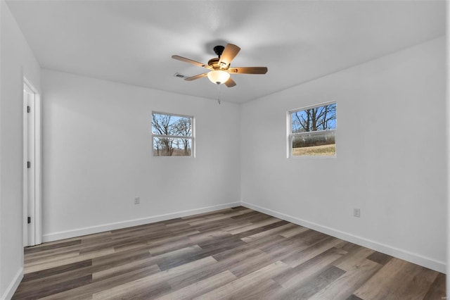 spare room with visible vents, wood finished floors, a ceiling fan, and baseboards