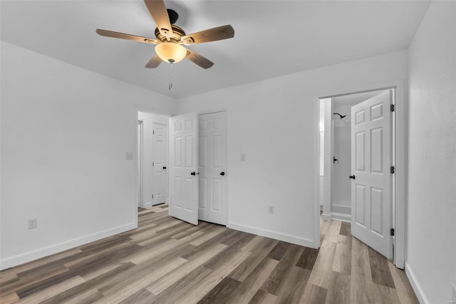 unfurnished bedroom featuring ensuite bath, baseboards, and wood finished floors