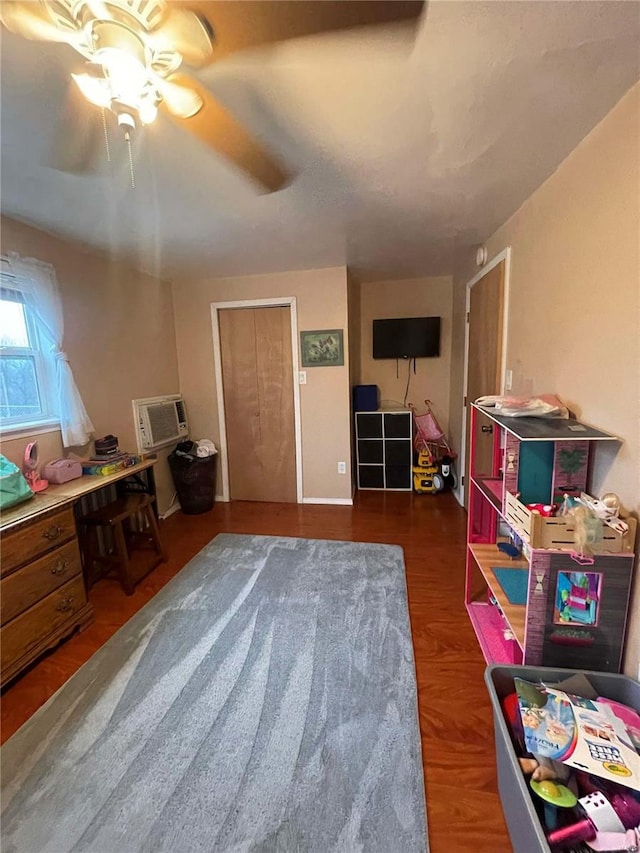 playroom featuring dark wood-type flooring, a wall unit AC, and ceiling fan