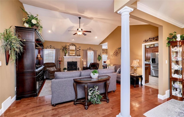 living room featuring ornate columns, vaulted ceiling, light wood-type flooring, ceiling fan, and a fireplace