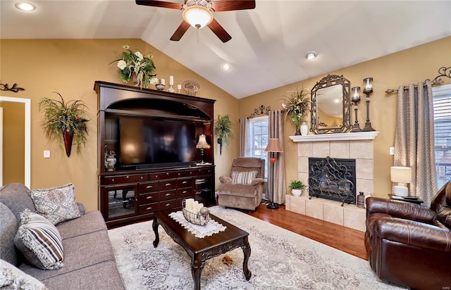 living room featuring ceiling fan, vaulted ceiling, a tile fireplace, and wood-type flooring