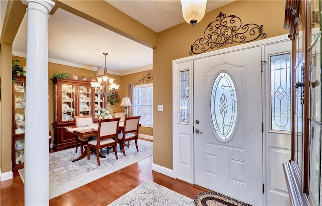 foyer featuring ornate columns, wood-type flooring, crown molding, and a notable chandelier