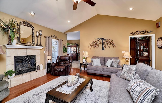 living room featuring a tiled fireplace, hardwood / wood-style floors, vaulted ceiling, and ceiling fan