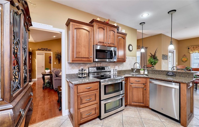 kitchen with dark stone countertops, decorative light fixtures, kitchen peninsula, and appliances with stainless steel finishes