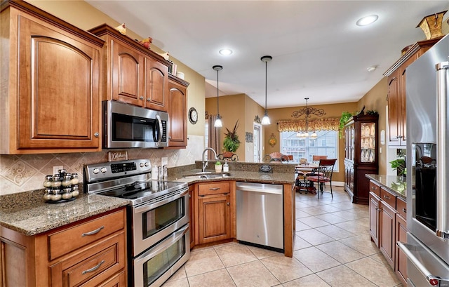 kitchen with sink, appliances with stainless steel finishes, kitchen peninsula, pendant lighting, and dark stone counters