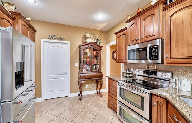 kitchen with stainless steel appliances, light tile patterned floors, backsplash, and light stone counters