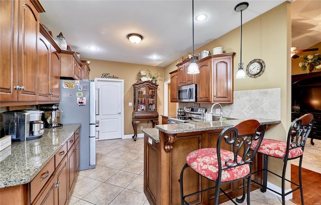 kitchen featuring a breakfast bar area, hanging light fixtures, stainless steel appliances, light stone countertops, and kitchen peninsula