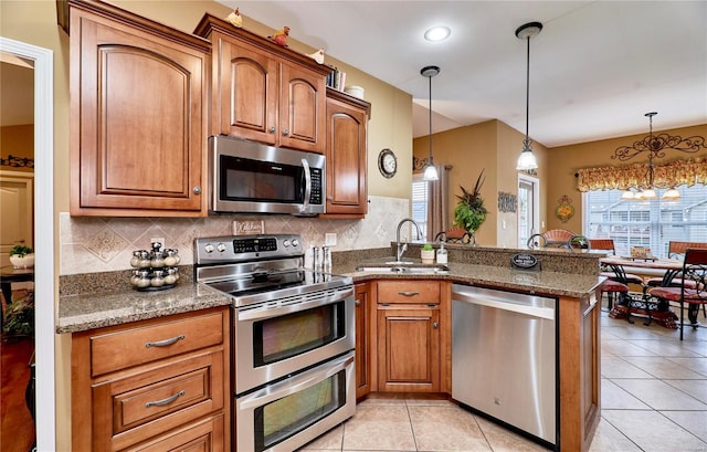 kitchen with stainless steel appliances, sink, dark stone counters, and decorative light fixtures