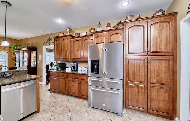 kitchen featuring dark stone countertops, decorative light fixtures, light tile patterned flooring, and appliances with stainless steel finishes