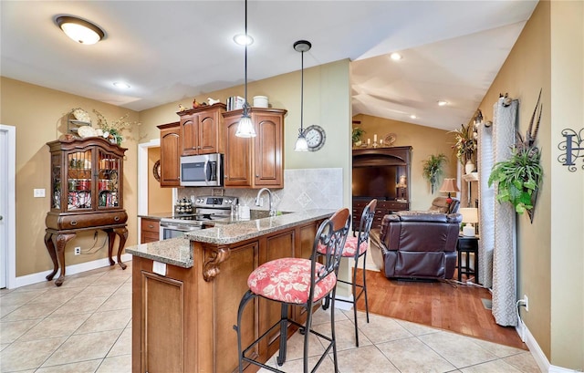 kitchen with light tile patterned flooring, a breakfast bar area, hanging light fixtures, appliances with stainless steel finishes, and kitchen peninsula