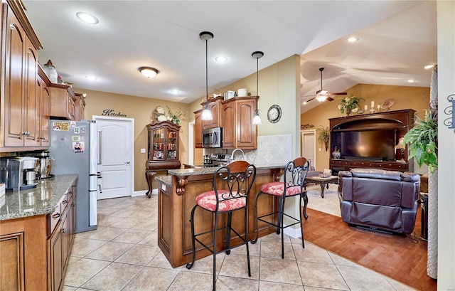 kitchen with pendant lighting, a kitchen bar, light stone counters, kitchen peninsula, and stainless steel appliances