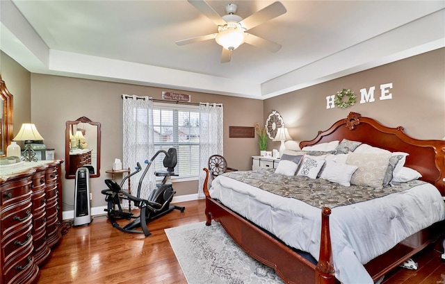 bedroom with ceiling fan, a tray ceiling, and hardwood / wood-style floors