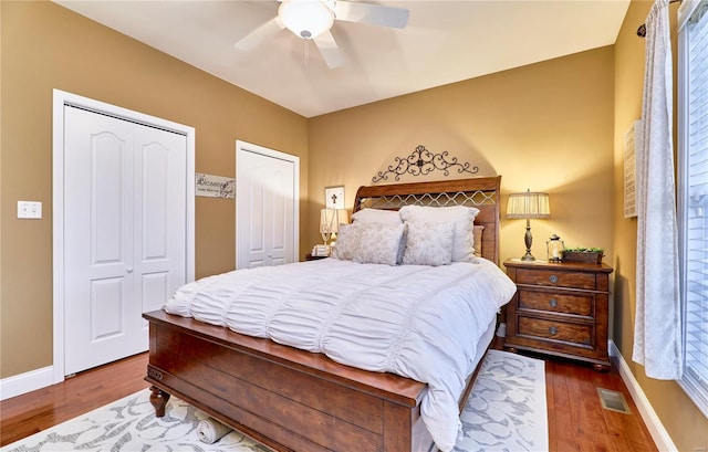 bedroom with two closets, hardwood / wood-style floors, and ceiling fan