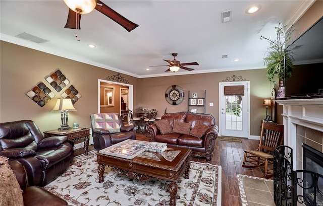 living room featuring a tile fireplace, hardwood / wood-style floors, ceiling fan, and crown molding