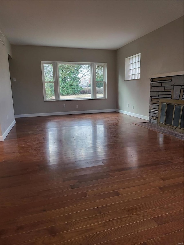 unfurnished living room with a stone fireplace, wood finished floors, and baseboards