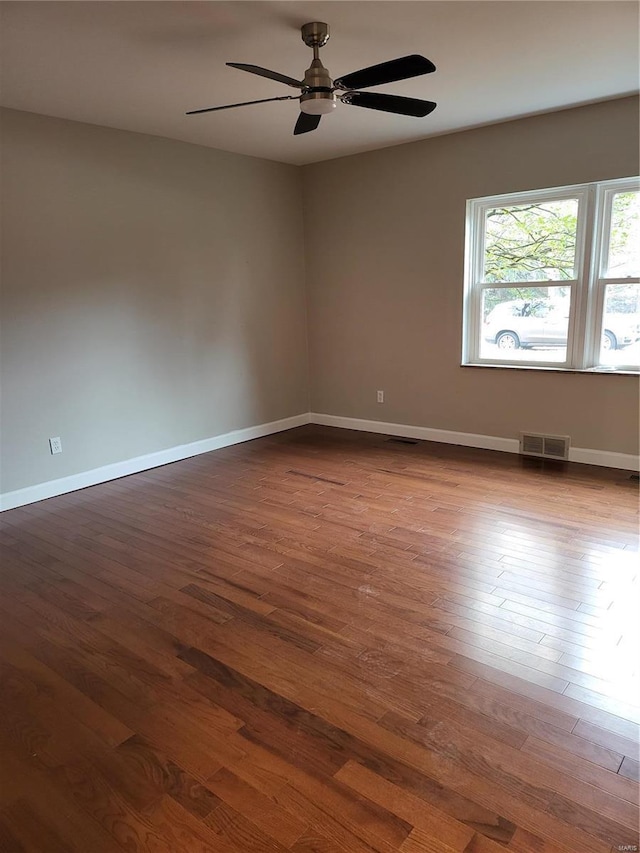 empty room featuring ceiling fan, dark wood finished floors, visible vents, and baseboards