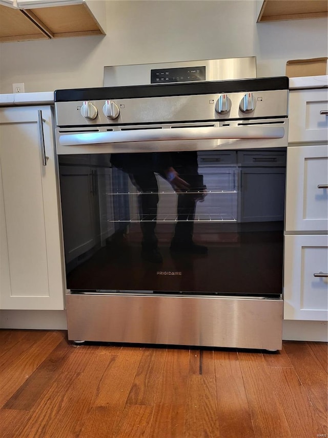 room details featuring light wood-style floors, white cabinets, and stainless steel electric range oven