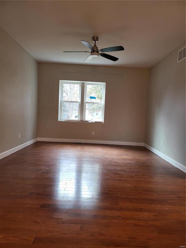 spare room with ceiling fan, visible vents, baseboards, and dark wood finished floors