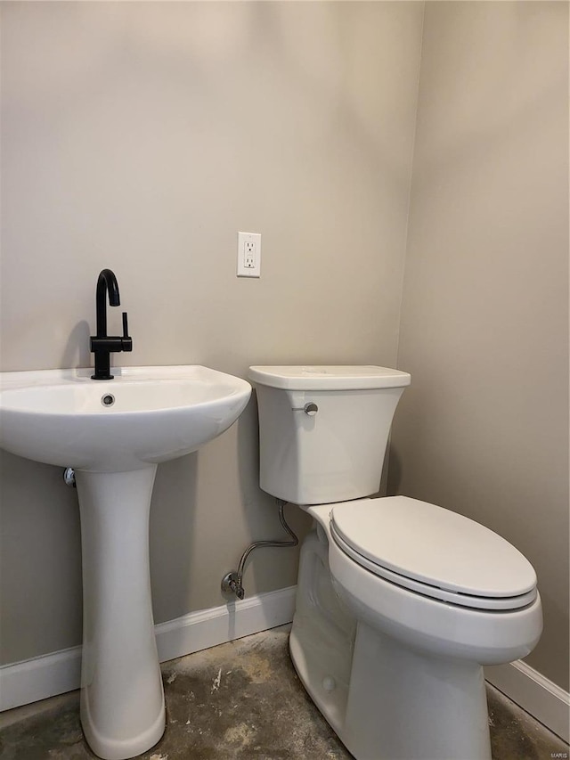 half bathroom with toilet, baseboards, concrete flooring, and a sink