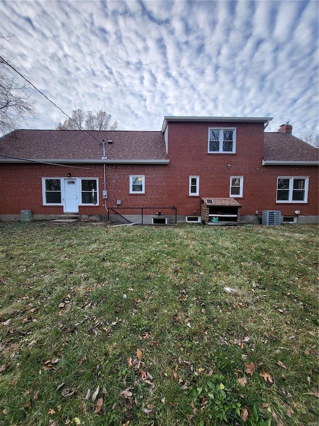 rear view of house with central AC, a yard, brick siding, and roof with shingles