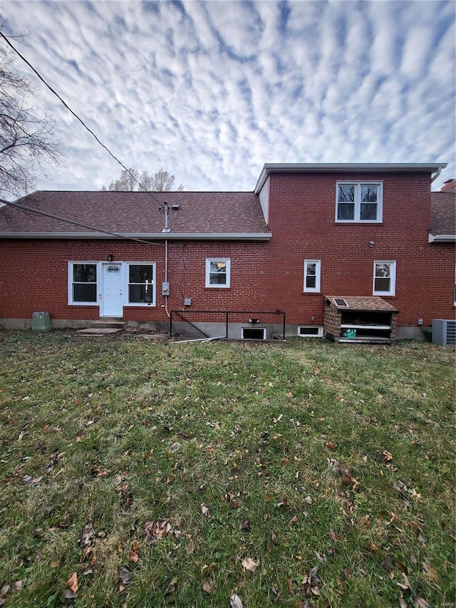 back of property with a shingled roof, cooling unit, brick siding, and a lawn