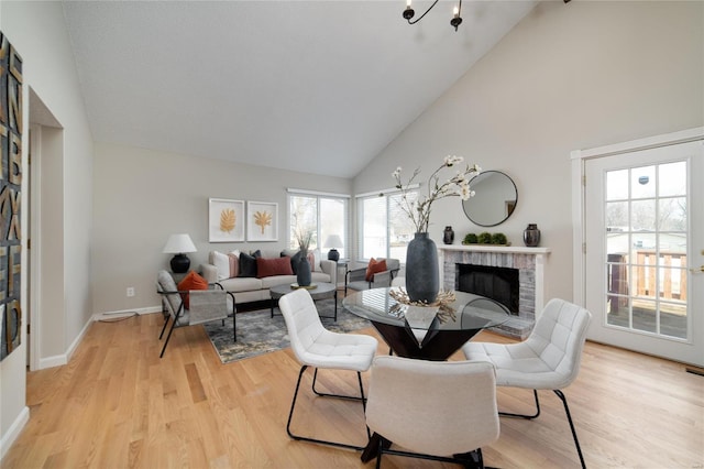 dining area with a brick fireplace, high vaulted ceiling, and light wood-type flooring