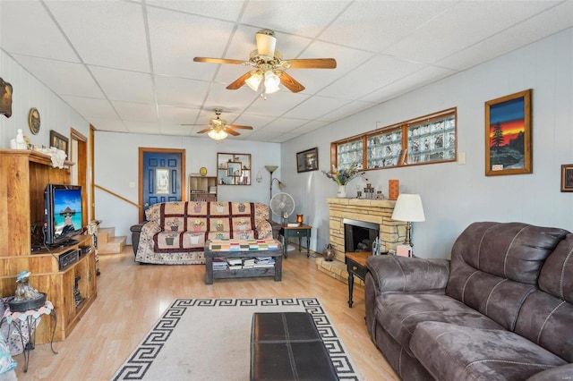 living room with ceiling fan, a stone fireplace, a paneled ceiling, and light hardwood / wood-style floors