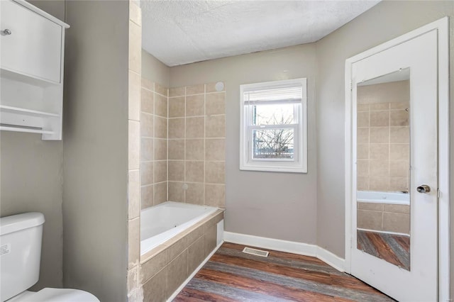 bathroom with hardwood / wood-style flooring, tiled shower / bath, a textured ceiling, and toilet