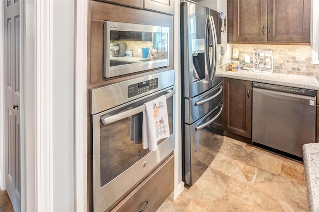 kitchen featuring stainless steel appliances, light stone countertops, dark brown cabinets, and backsplash